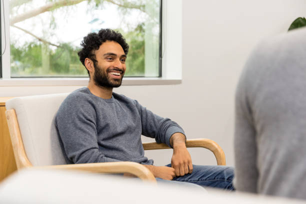 Young adult male patient smiles during his therapy appointment The young adult male patient smiles while listening to his mental health therapist. office buddies stock pictures, royalty-free photos & images