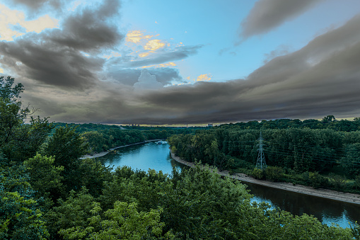 Wide view of the Mississippi River shore, outside of Minneapolis. Minnesota, Along the river shore are power pylons and electrical wires that follow the river.  On both sides of the river is dense vegetation and in the sky above are clouds from an impending storm,\n\nTaken in Minneapolis. Minnesota, USA