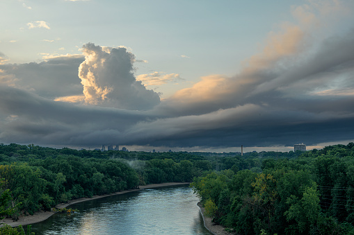 Wide angle view of the Mississippi River shore, outside of Minneapolis. Minnesota, Along the river shore are power pylons and electrical wires that follow the river.  On both sides of the river is dense vegetation and in the sky above are clouds from an impending storm,\n\nTaken in Minneapolis. Minnesota, USA