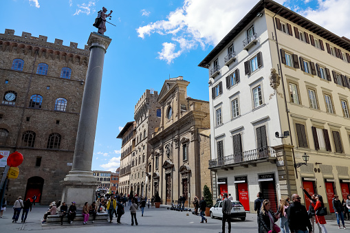 Florence, Italy - April 16, 2023: Piazza Santa Trinita, the Column of Justice, Basilica di Santa Trinita and other buildings surrounding the square. There are many people in the square