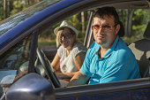 Cute man and woman are smiling from the inside of the car traveling around the country. Tourists enjoy auto travel while sitting in the car. The concept of traveling by car.