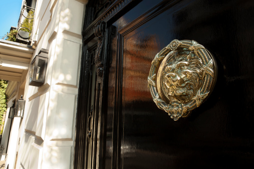 Black gloss door with brass door knocker of a lion. Lovely spring time sunshine and reflection in the gloss black door. Central Mayfair, London