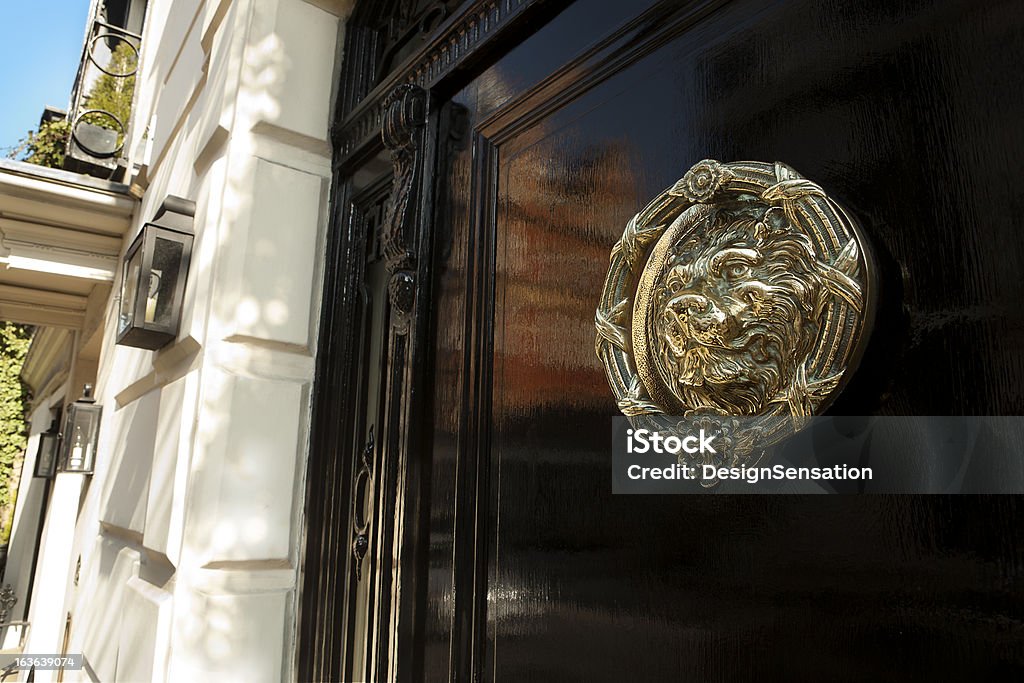 Brass door knocker, Mayfair, London XXXL Black gloss door with brass door knocker of a lion. Lovely spring time sunshine and reflection in the gloss black door. Central Mayfair, London Mayfair Stock Photo