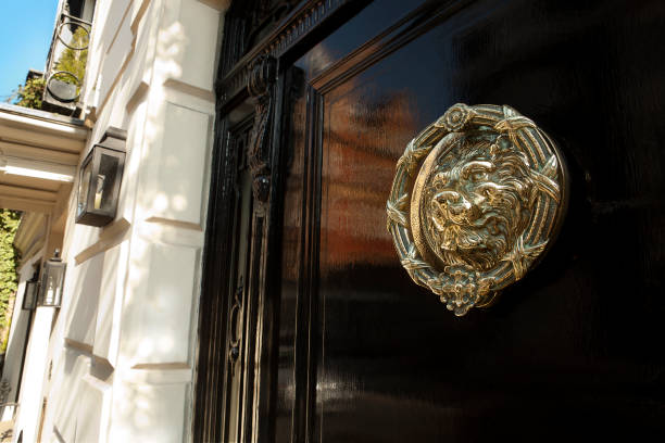 Brass door knocker, Mayfair, London XXXL Black gloss door with brass door knocker of a lion. Lovely spring time sunshine and reflection in the gloss black door. Central Mayfair, London Mayfair stock pictures, royalty-free photos & images