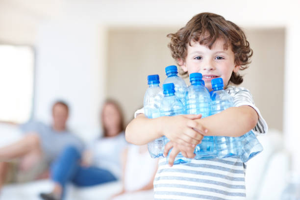 His parents stress the importance of recycling Young boy holding empty water bottles with his parents sitting in the background plastic bottles stock pictures, royalty-free photos & images