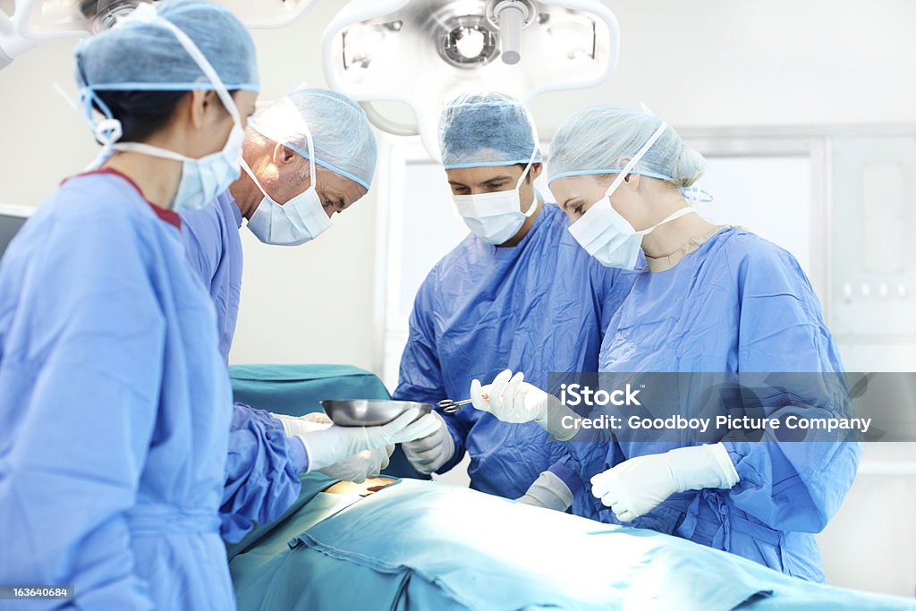 Trusted medical staff Nurse passing an instrument to a doctor while a group of medical professionals work in surgery Accidents and Disasters Stock Photo