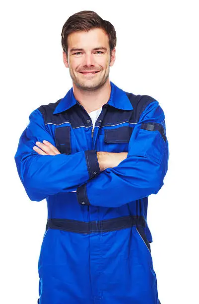 A studio shot of a smiling mechanic standing with his arms folded isolated on white