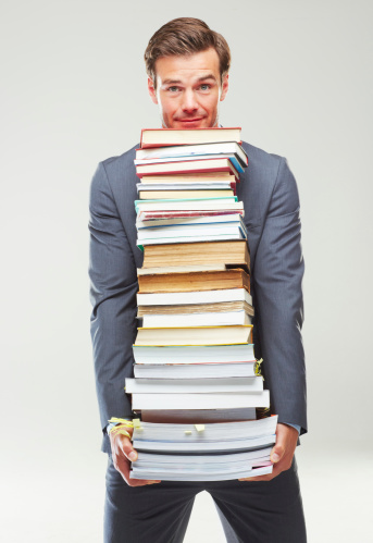 A studio shot of a well dressed young man carrying a stack of books in his arms isolated on white