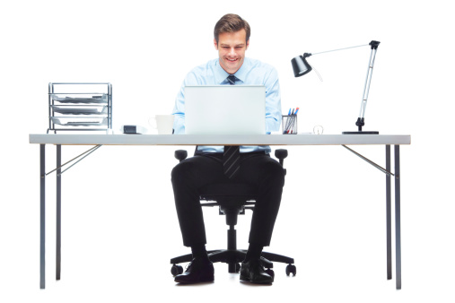 Studio shot of a cheerful-looking young businessman sitting in front of a laptop at an office desk