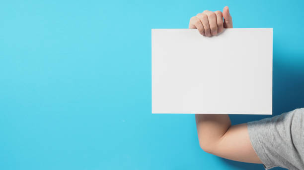 istock man hands is holding blank empty A4 paper on blue background. 1636411260