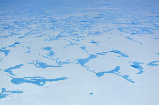 Greenland: melt ponds pattern in the ice sheet, aerial view - melt ponds are pools of water that form on the ice in the warmer months of spring and summer. Being generally darker than the surrounding ice and therefore having a lower albedo, melt ponds absorb solar radiation instead of reflecting it and therefore affect the Earth's radiation balance. Research shows that snowfall can no longer replenish the melted ice that flows into the ocean from Greenland’s glaciers. Since 2000 Greenland's melting ice added a millimetre a year to rising sea levels. A climate change causing the total loss of the ice sheet would raise sea levels by over seven metres, re-shaping the world's map.