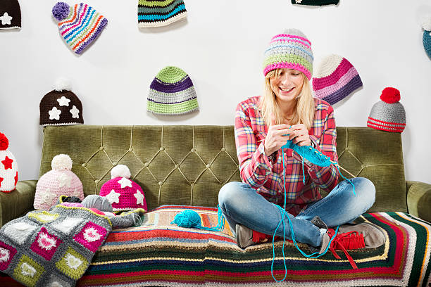 young woman knitter portrait on couch with winter hats - relaxation working humor sofa - fotografias e filmes do acervo