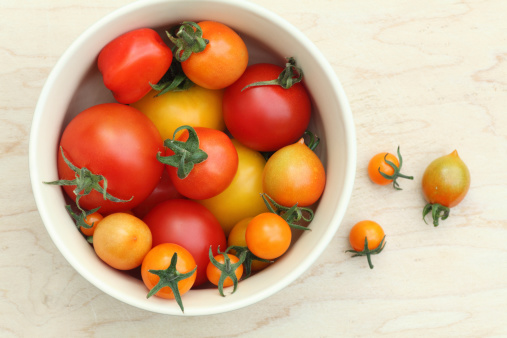 Red and yellow large and small tomatoes in a bowl with copy space