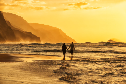 Silhouette of a couple at sunset walking along a Hawaiian beach.