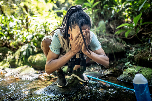 Young man washing his face during hiking in the forest