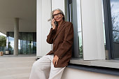 confident mature old lady with gray hair in glasses wearing a brown jacket is waiting for a call from a business partner