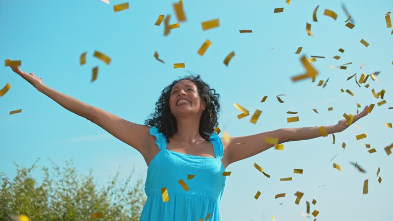 SLO MO Woman raising her hands towards the sky and smiling as confetti fly around