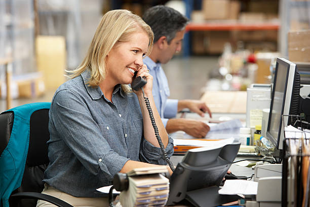 Businesswoman Working At Desk In Warehouse Businesswoman Working At Desk In Warehouse Smiling small office stock pictures, royalty-free photos & images