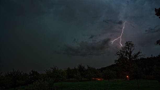 istock Scenic landscape with meadow and fruit trees with by night with lightning. 1636549400