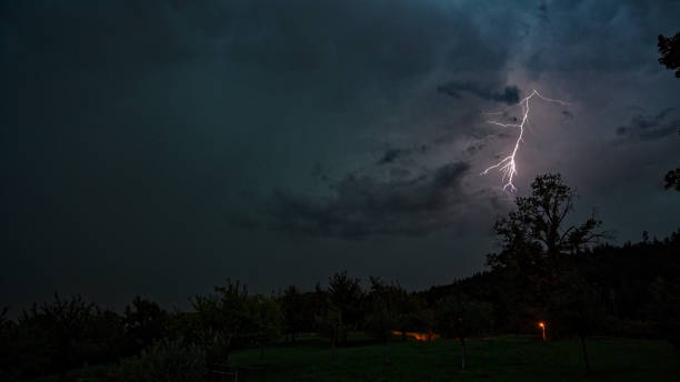 istock Scenic landscape with meadow and fruit trees with by night with lightning. 1636549401