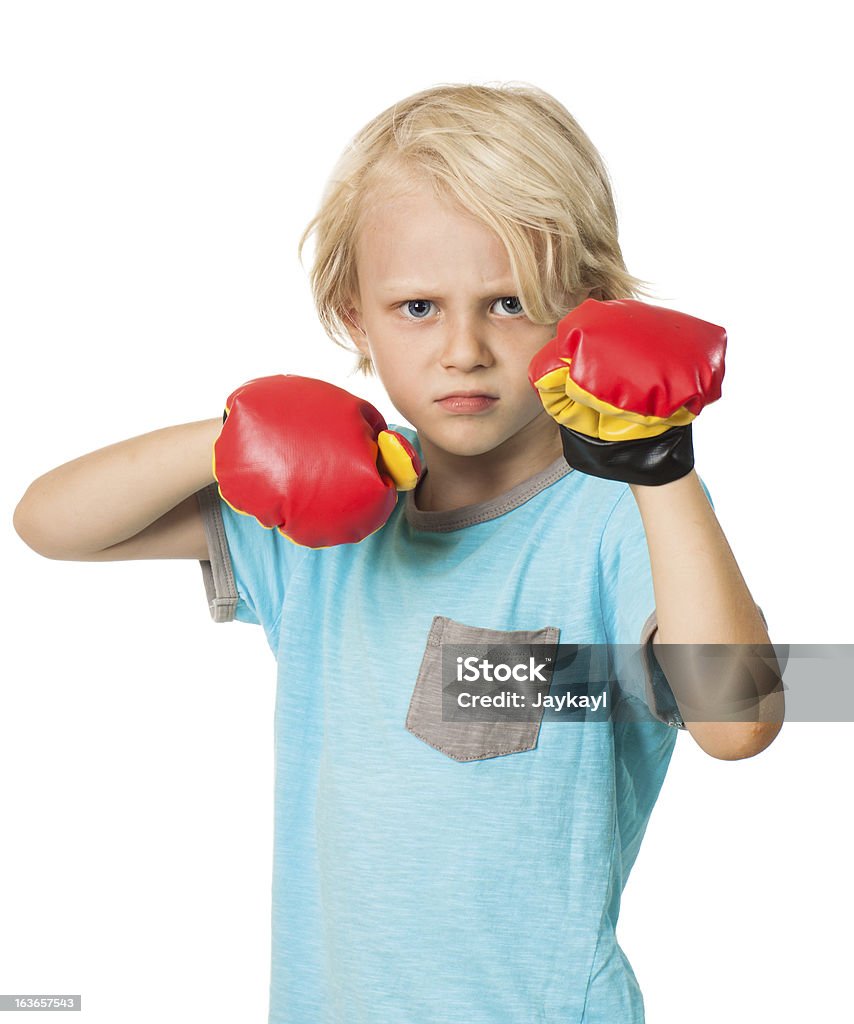 Serious angry boy with boxing gloves A serious and determined young boy wearing boxing gloves and looking at the camera. Isolated on white. Aggression Stock Photo
