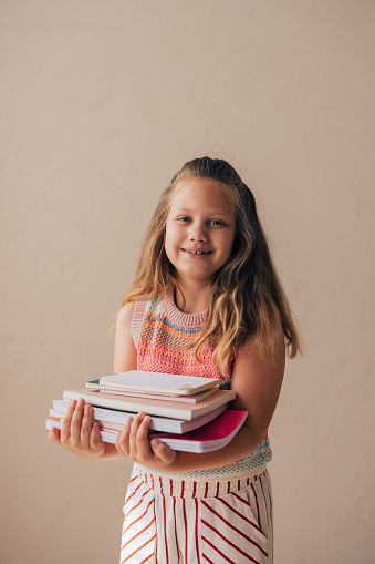 A portrait of a cute smiling schoolgirl holding her books and notebooks on a first day of school.