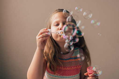 A portrait of a smiling schoolgirl playing with soap bubbles.