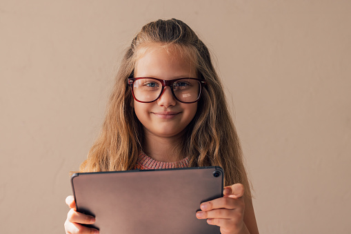 A portrait of a smiling blonde schoolgirl with glasses holding a digital tablet.