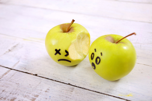 Close up of one bitten apple and another apple with comic painted face looking worried.