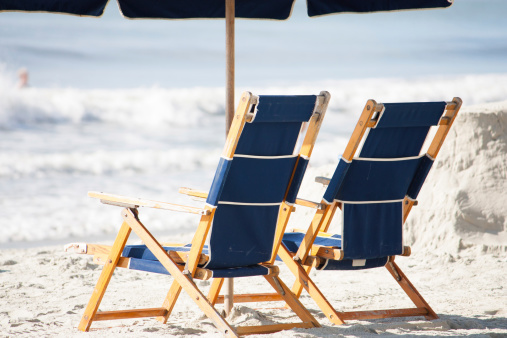 two luxury beach chairs sit under an umbrella on the sunny beach
