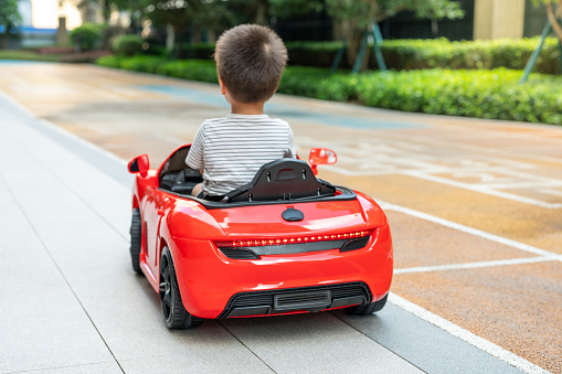 Cute multiracial toddler boy looks around while riding a red remote controlled car on a paved track