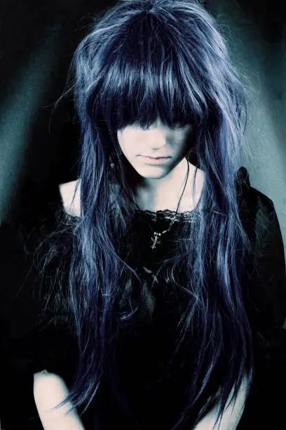 Portrait of a young woman with messy long hair, wearing a beautiful gothic dress, looking down.