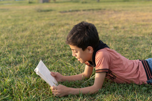 istock Boy reading a book in the green grass. 1636696909