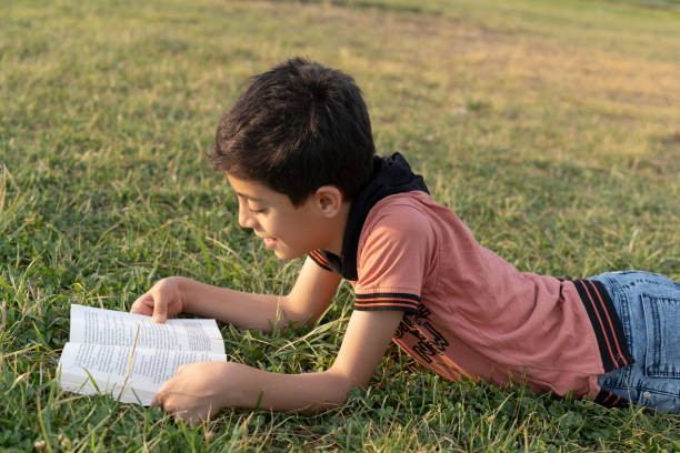 istock Boy reading a book in the green grass. 1636697416