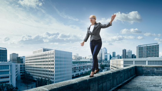 Business woman walking on the edge of a roof with the city at the background.