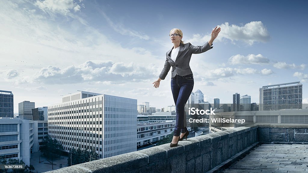 Business risks. Business woman walking on the edge of a roof with the city at the background. Balance Stock Photo