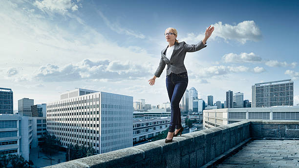 Business risks. Business woman walking on the edge of a roof with the city at the background. tightrope stock pictures, royalty-free photos & images