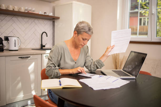 istock Mature woman using calculator while going through bills and home finances 1636765243