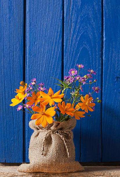 Colourful flowers in a burlap sack covered vase, in front of an old window shutter.