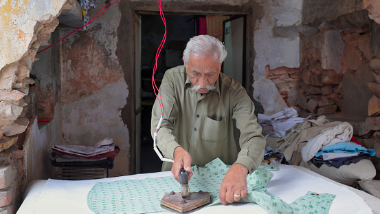 Senior Indian man ironing clothes in Jaipur. Jaipur is known as the Pink City, because of the color of the stone exclusively used for the construction of all the structures.
