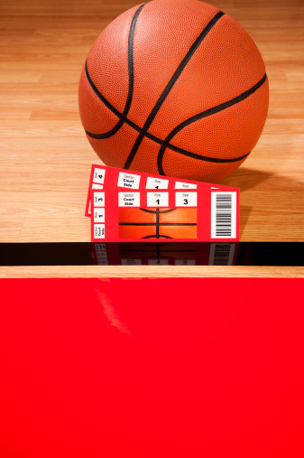 A pair of Court Side ticket stubs sitting against a basketball  on a hardwood court