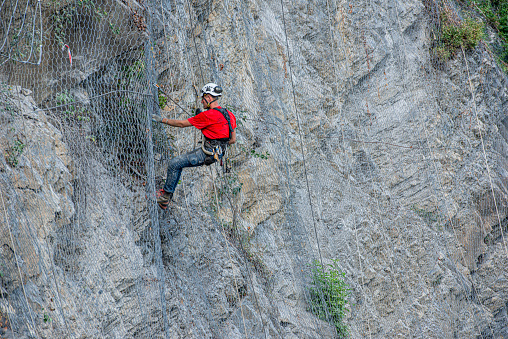 Dossena Italy August 24th 2023:Climber placing safety nets to avoid falling rocks