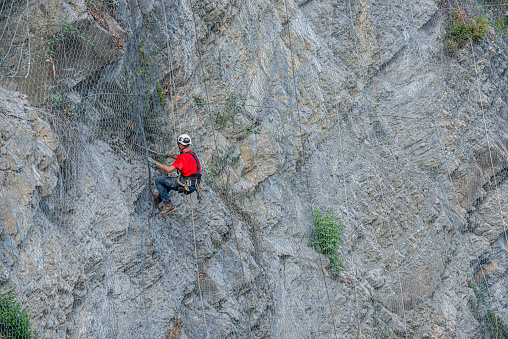 Dossena Italy August 24th 2023:Climber placing safety nets to avoid falling rocks