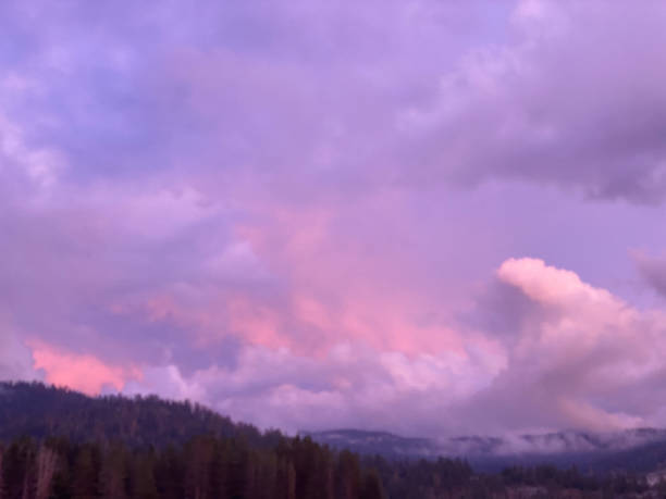 dramatic cloudscape of storm clouds at sunset. Purple, lavender, pink and gray colors over the silhouette of the mountain range stock photo