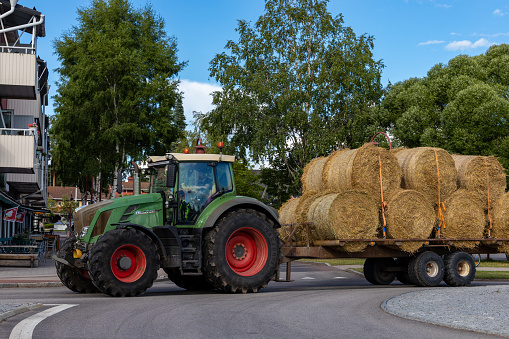 Rattvik, Sweden July 14, 2023 A tractor drives hay bales down the street on a trailer.