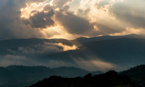 istock Bright sun rays light shining through dark clouds over mountain at sunset. Dramatic sky in winter 1636878422
