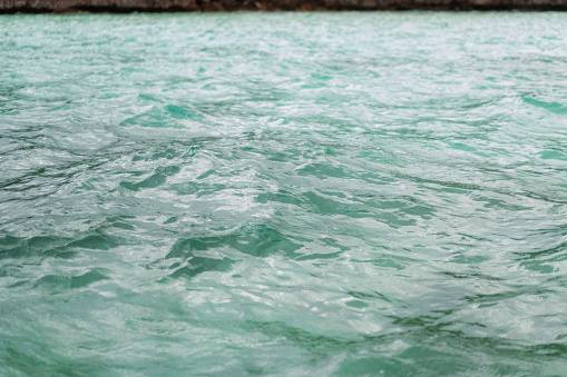 Close up detail of powerful teal blue wave breaking in open ocean on a bright sunny afternoon