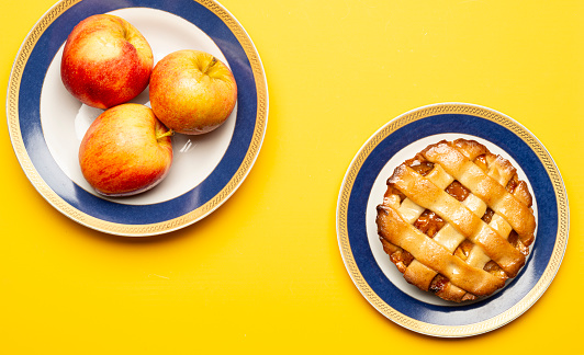 High angle view of delicious apple pie with three organic red apple fruit on plate over a yellow background. Image made in studio.