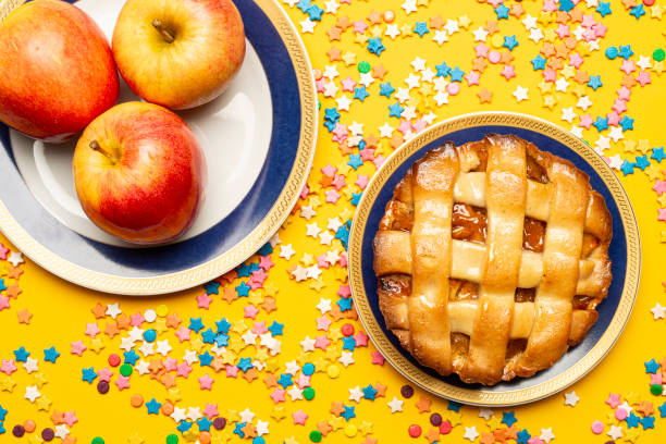 High angle view of delicious apple pie and red apple fruits on plate over a yellow color background with sugar sprinkles to celebrate a birthday at home.