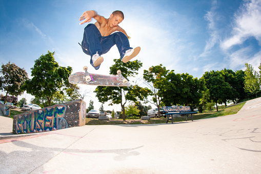 Active mature Caucasian male jumping with a skate in a public park. He is fit and healthy. He is wearing casual clothes on a sunny summer day.